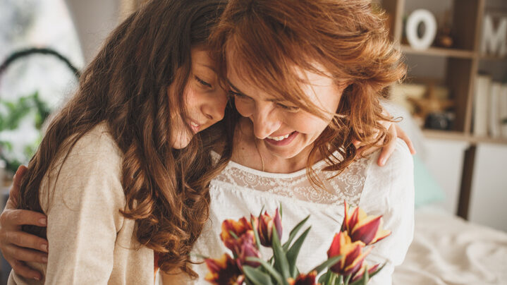 Happy mother and daughter hugging and holding a bouquet of fresh flowers